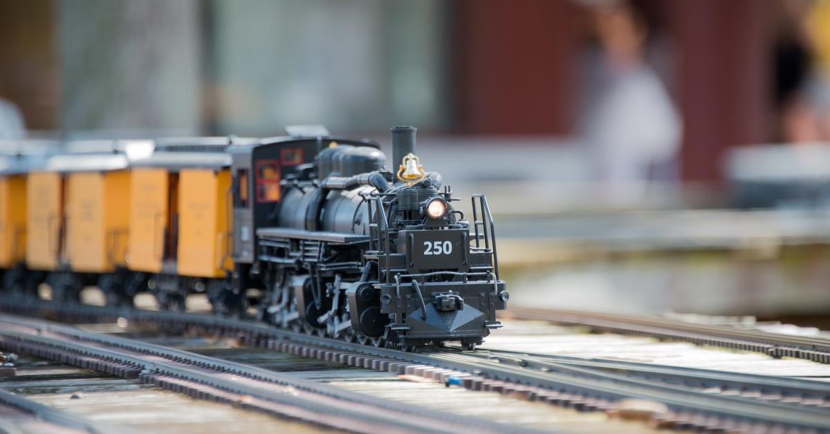 A model train with the number '250' on the front drives down a model train track, hauling orange containers.